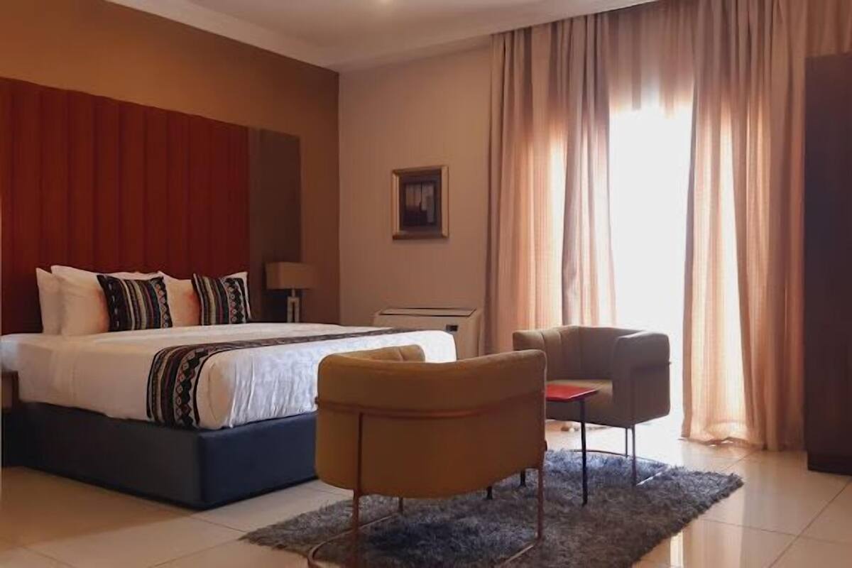 A hotel room with a large bed, a desk, two chairs, and a wardrobe.