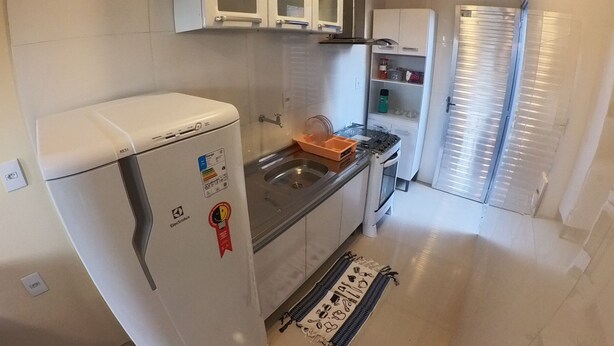 Une cuisine de taille réduite avec des meubles blancs, un réfrigérateur, une cuisinière et un évier.