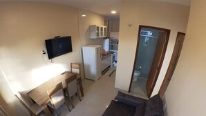 Un espace de vie compact comprenant un canapé, une table à manger avec des chaises, un téléviseur fixé au mur, un réfrigérateur et un coin cuisine avec des placards et un four à micro-ondes.