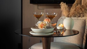 Une pièce moderne avec une table en verre dressée pour un repas, un fauteuil confortable et un téléviseur en arrière-plan.