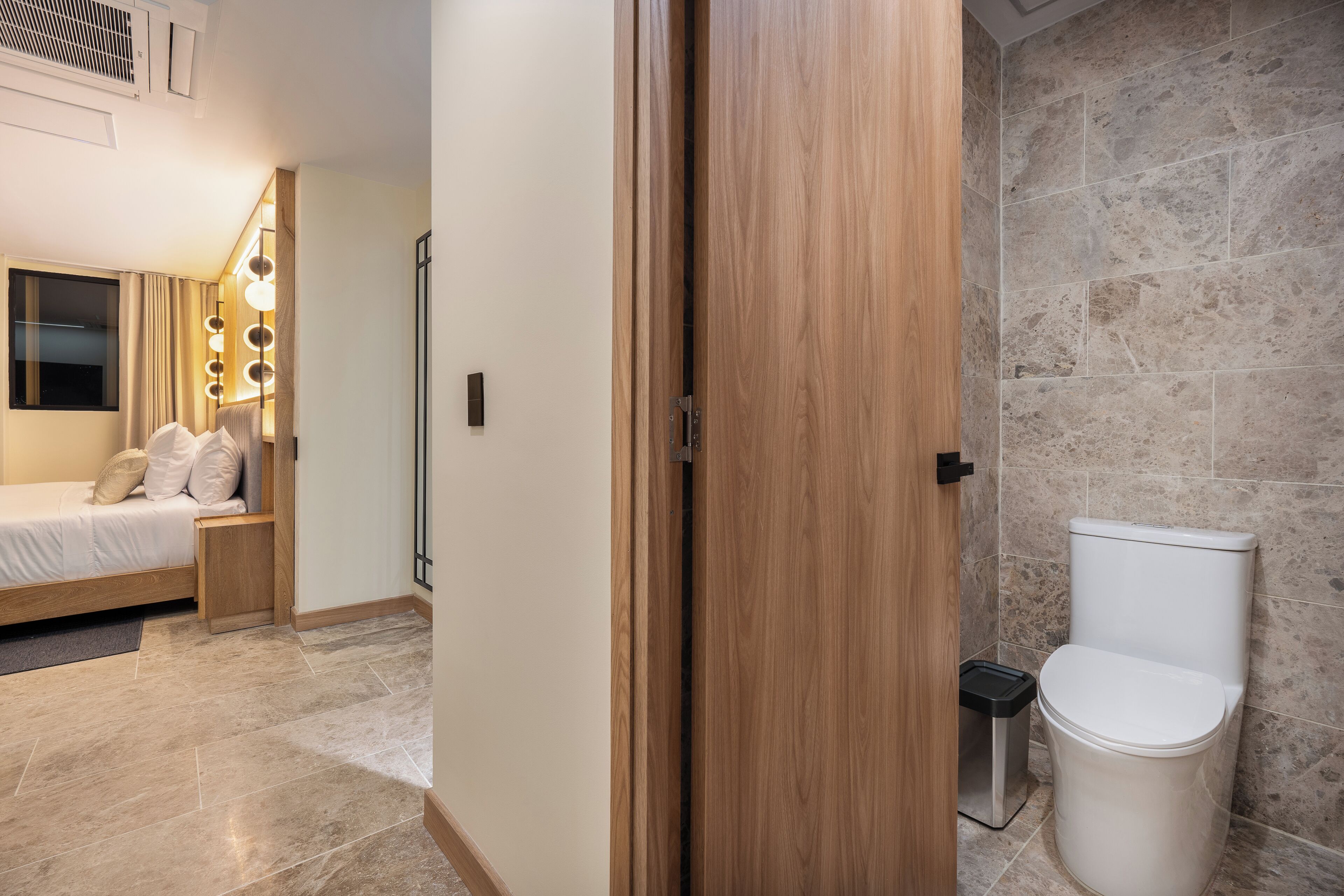 Una habitación de hotel con cama, mesita de noche y baño con inodoro y ducha.