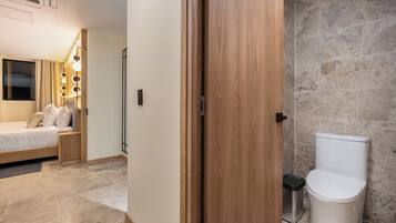 Una habitación de hotel con cama, mesita de noche y baño con inodoro y ducha.