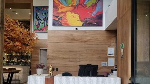 A reception desk with a colorful abstract painting above it, a wooden panel wall, and a glass door to the right. - LIN Boutique Hotel by HOUSY HOST (Medellín)