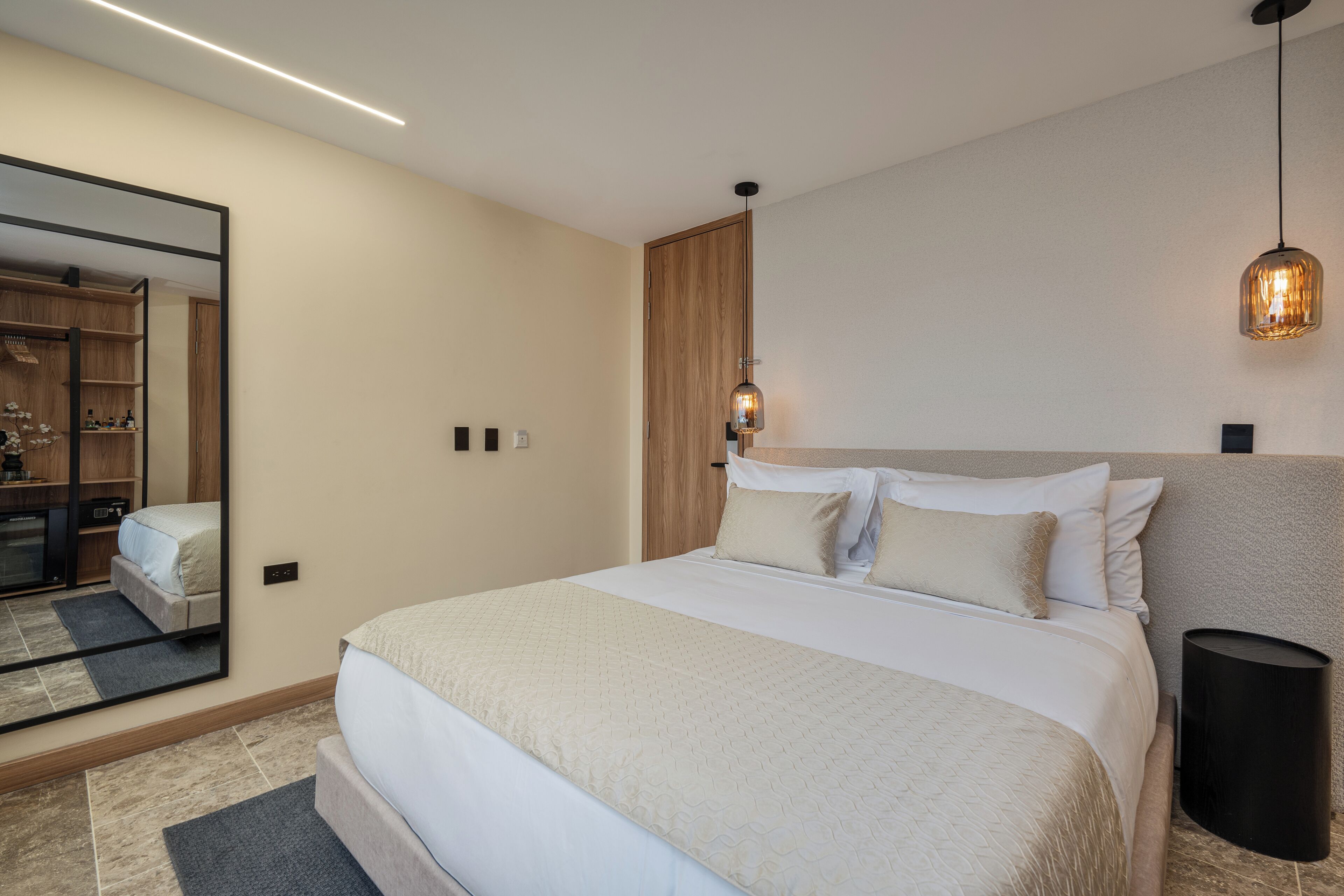 A modern bedroom with a large bed, a wardrobe, a mirror, and a bedside lamp.