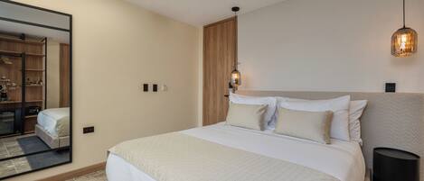 A modern bedroom with a large bed, a wardrobe, a mirror, and a bedside lamp.