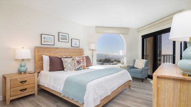 Une chambre à coucher avec un lit en bois, une table de chevet, une chaise et une vue sur la mer par la fenêtre.