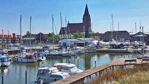 A marina with boats docked, a church with a tall steeple, and residential buildings in the background. - Hausboot in Barth am Barther Bodden (Barth)