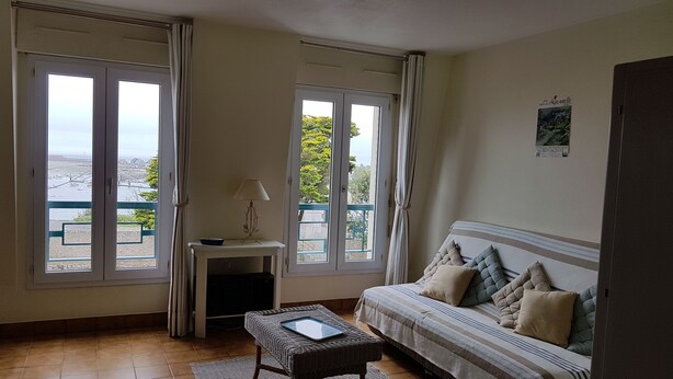 A room with a sofa, a small table with a lamp, and a view of the sea through large windows. - Apartment rental, sea view, Port-Louis (56), 3-star CLEVACANCES label (Port-Louis)