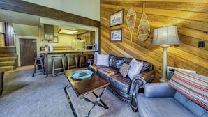 A cozy living room with a leather sofa, a coffee table, and a kitchen in the background.