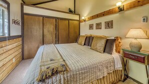 A bedroom with a large bed, wooden walls, a nightstand with a lamp, and a small plant.