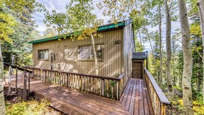 A wooden cabin with a deck, surrounded by trees.