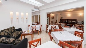 A spacious dining area with multiple tables and chairs, a sofa, and a kitchen area visible through an open doorway. - Holiday studio close to the seaside beach (Rewal)