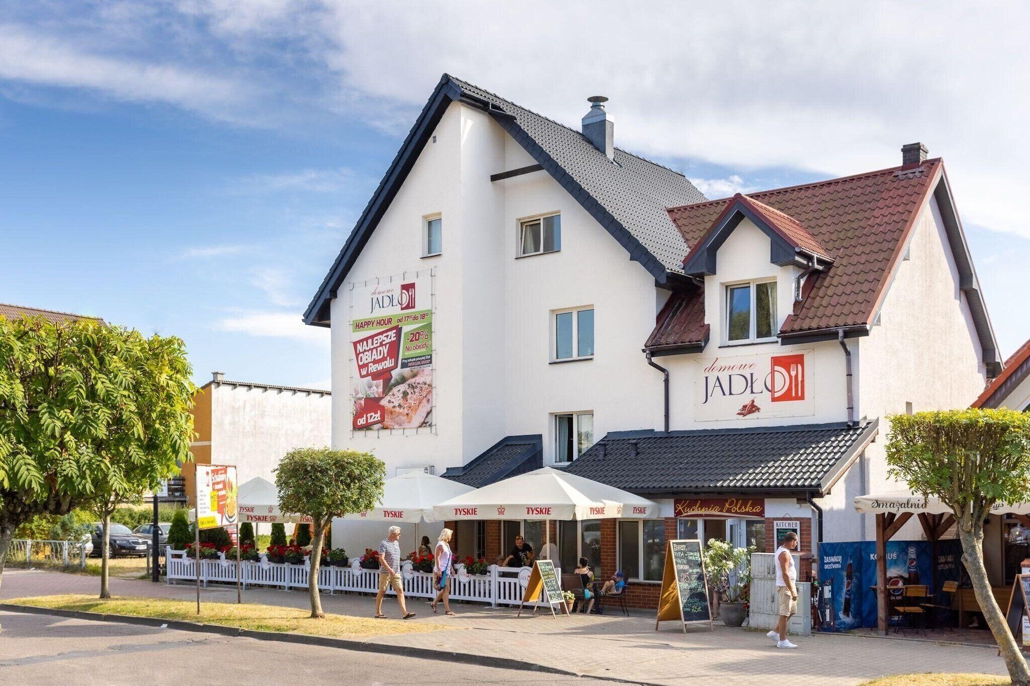 A two-story building with a white facade and a red-tiled roof. There are outdoor seating areas with umbrellas and a sign that reads "JADLO 11".