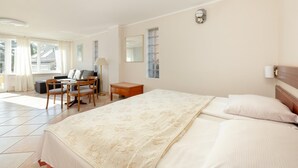 A hotel room with a large bed, a desk with a chair, a small table, and a window with curtains. - Comfortable holiday studio, breakfast included (Rewal)