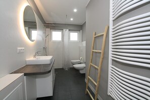 Et moderne badeværelse med håndvask, spejl, bruser, toilet og en træstige.