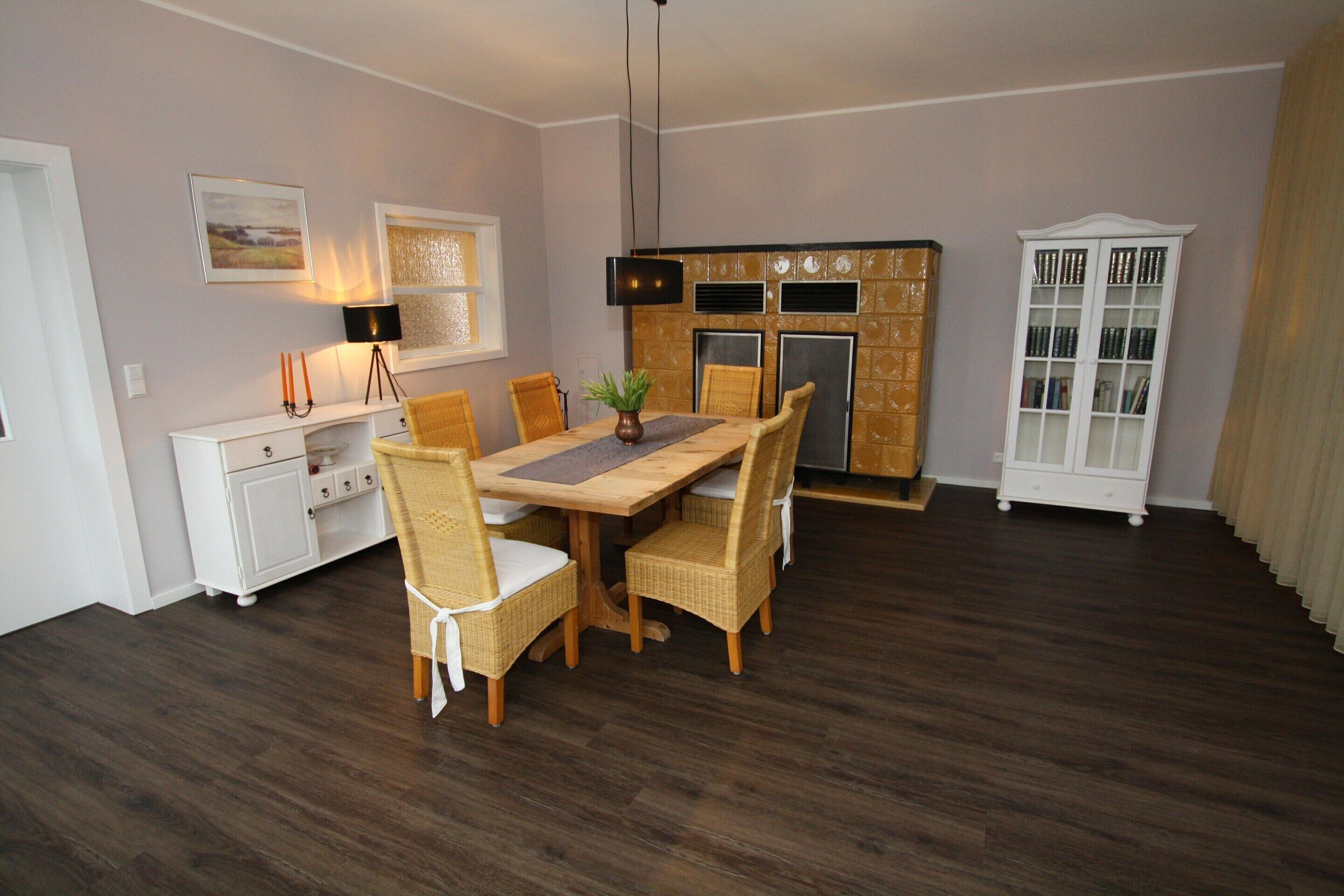 A dining area with a wooden table and wicker chairs, a white cabinet, and a bookshelf.