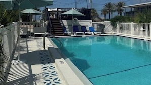 Ein Swimmingpool mit weißer Liegefläche, Sonnenschirmen und Liegestühlen.