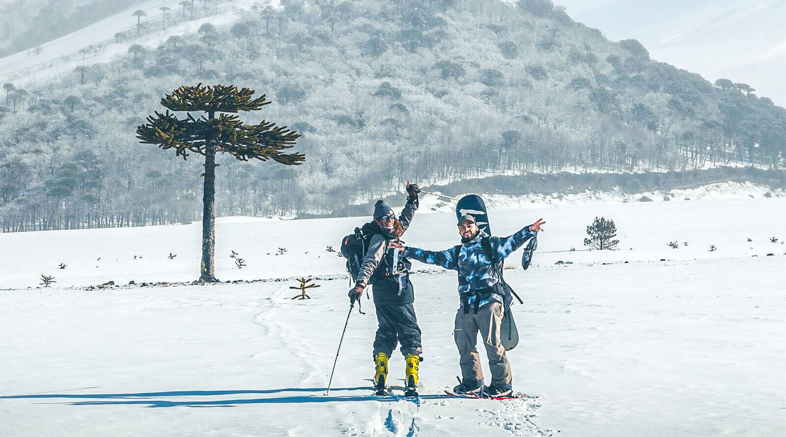 Deux personnes font du ski dans un paysage enneigé, avec une montagne en arrière-plan.