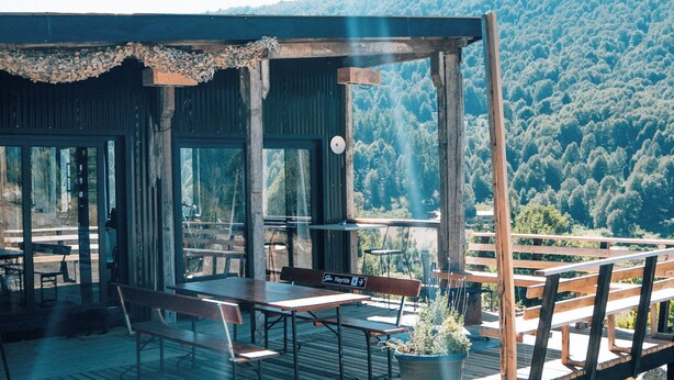A wooden deck with picnic tables and benches overlooking a forested hillside. - K10 Lodge (Curacautin)