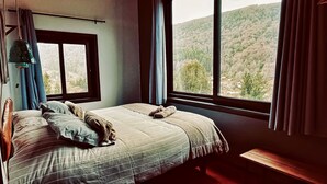 A bedroom with a large bed, a window, and a view of a forest. - K10 Lodge (Curacautin)