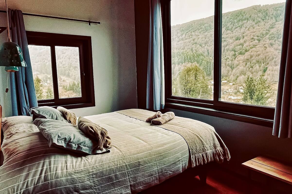 A bedroom with a large bed, a window, and a view of a forest.
