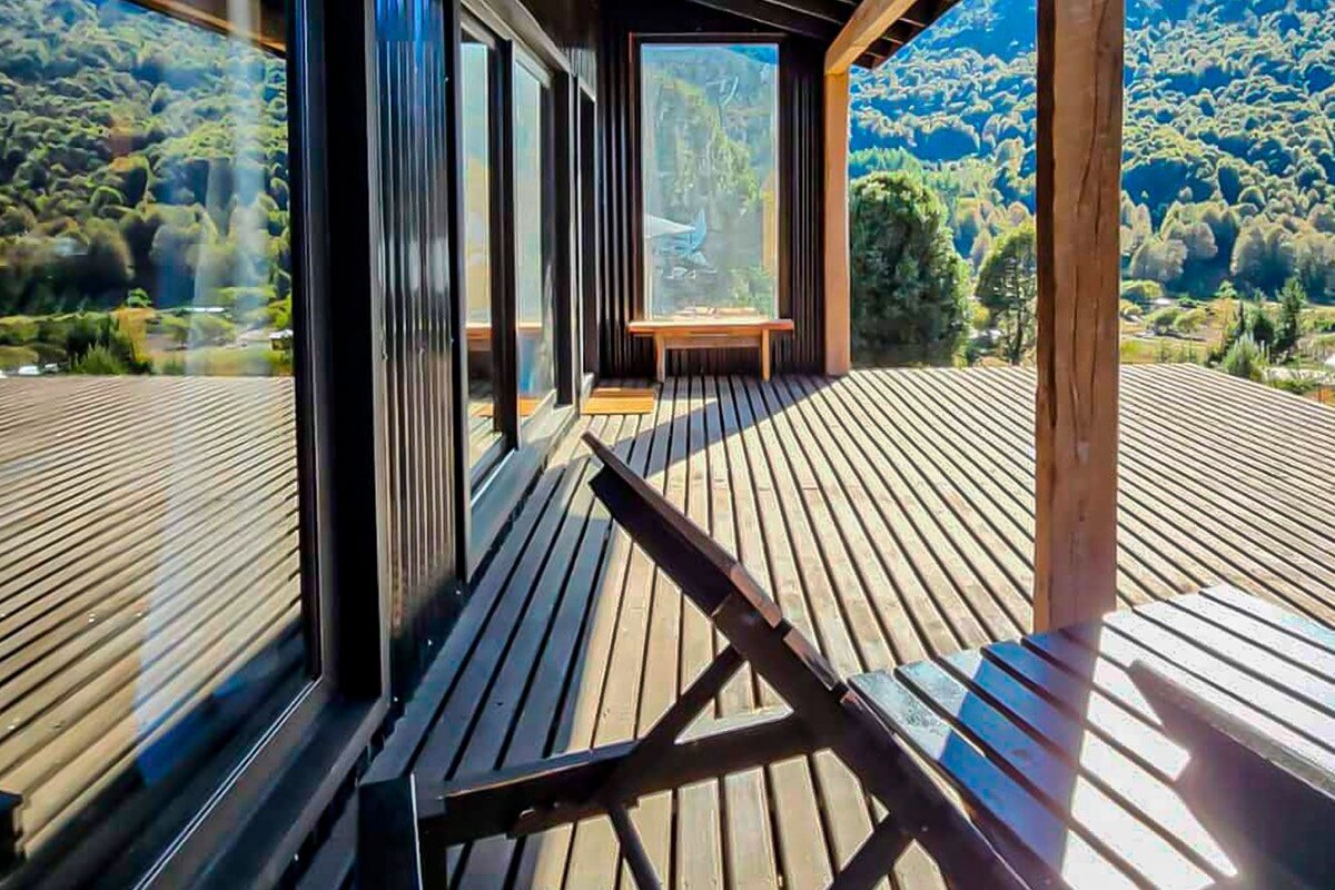 Un terrazzo in legno con una panchina e un tavolo, affacciato su un pendio boscoso.