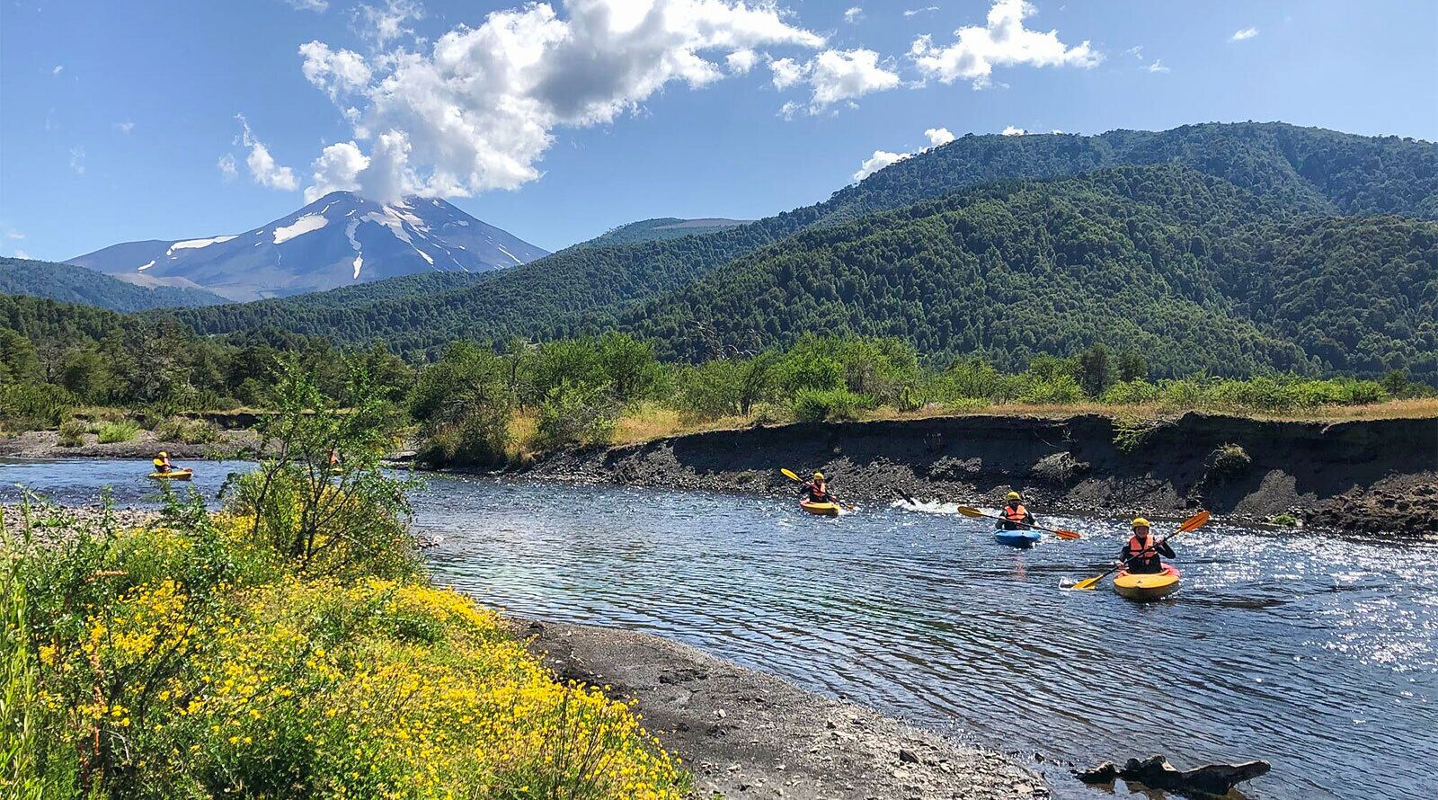 Kayakers on a river surrounded by greenery and a mountain in the background.
