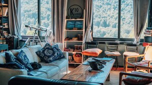 A cozy living room with a sofa, a coffee table, and a bookshelf. There is a telescope and a fan on a table. - K10 Lodge (Curacautin)