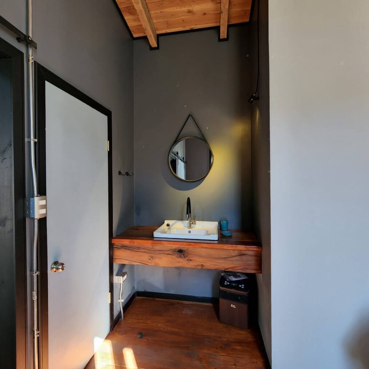 Un baño pequeño con tocador de madera, un espejo redondo y un cubo de basura.