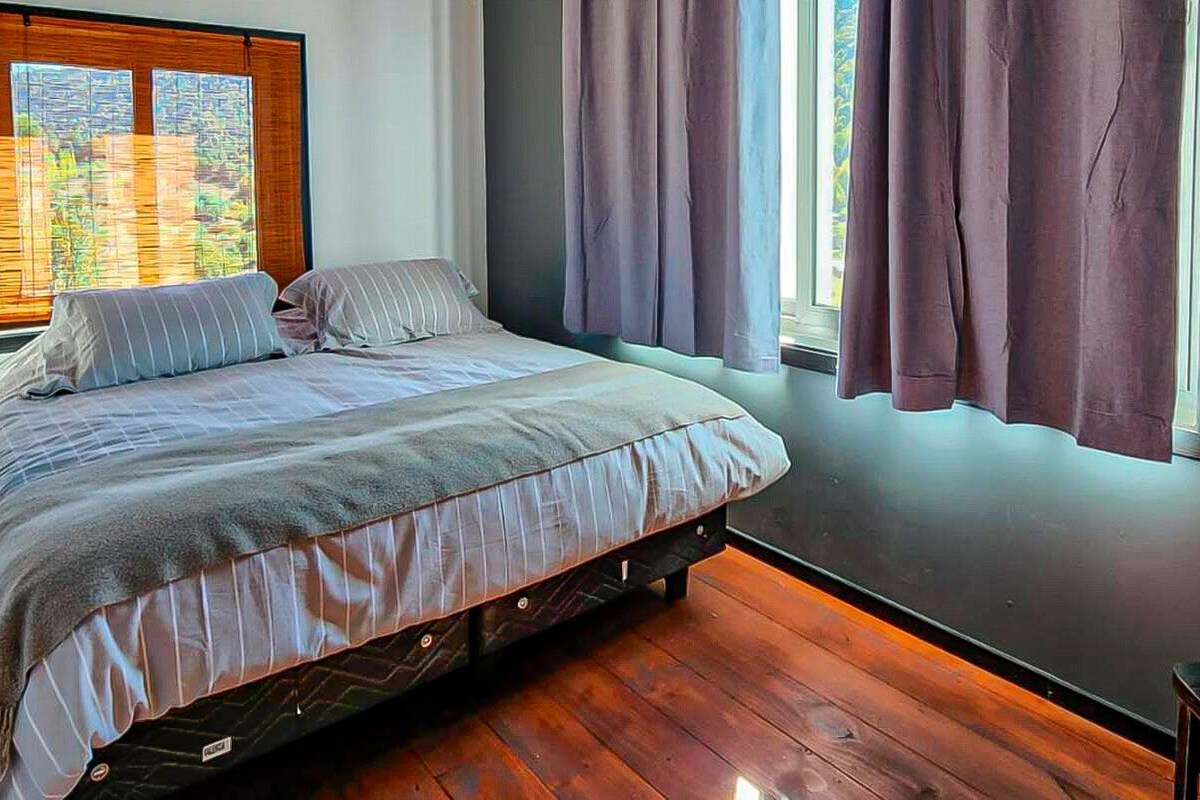 A bedroom with a bed, a window with curtains, and a view of the outdoors.