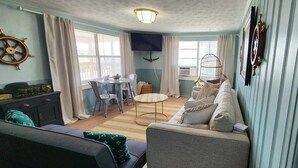 Un espace de vie compact comprenant un canapé, une table à manger avec des chaises, un téléviseur fixé au mur et un fauteuil suspendu.