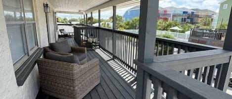 A covered porch with a dark wooden floor, a wicker sofa, and a railing.