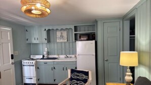 Une cuisine compacte équipée d’une cuisinière, d’un four à micro-ondes et d’un réfrigérateur, avec des meubles de couleur bleu clair et un lustre en osier.