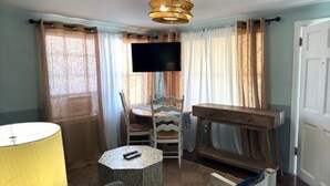 Une pièce avec un téléviseur fixé au mur, une chaise en bois, une petite table ronde et une lampe.