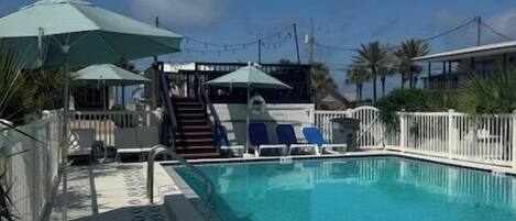 Una piscina con deck blanco, sombrillas y sillas de descanso.