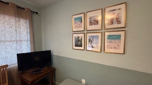 Una sala de estar con una televisión de pantalla plana sobre un pedestal de madera, una mesita y seis cuadros enmarcados en la pared.