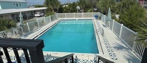 Piscina rectangular con cubierta de madera y barandillas, rodeada por una valla blanca y palmeras.