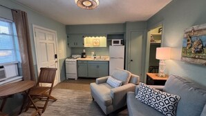 A compact living space with a kitchenette, a dining area with a table and chairs, and a seating area with a sofa and cushions.