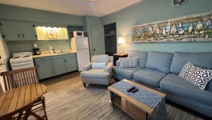 A compact living space with a kitchenette, a sofa set, a wooden table, and a patterned rug.