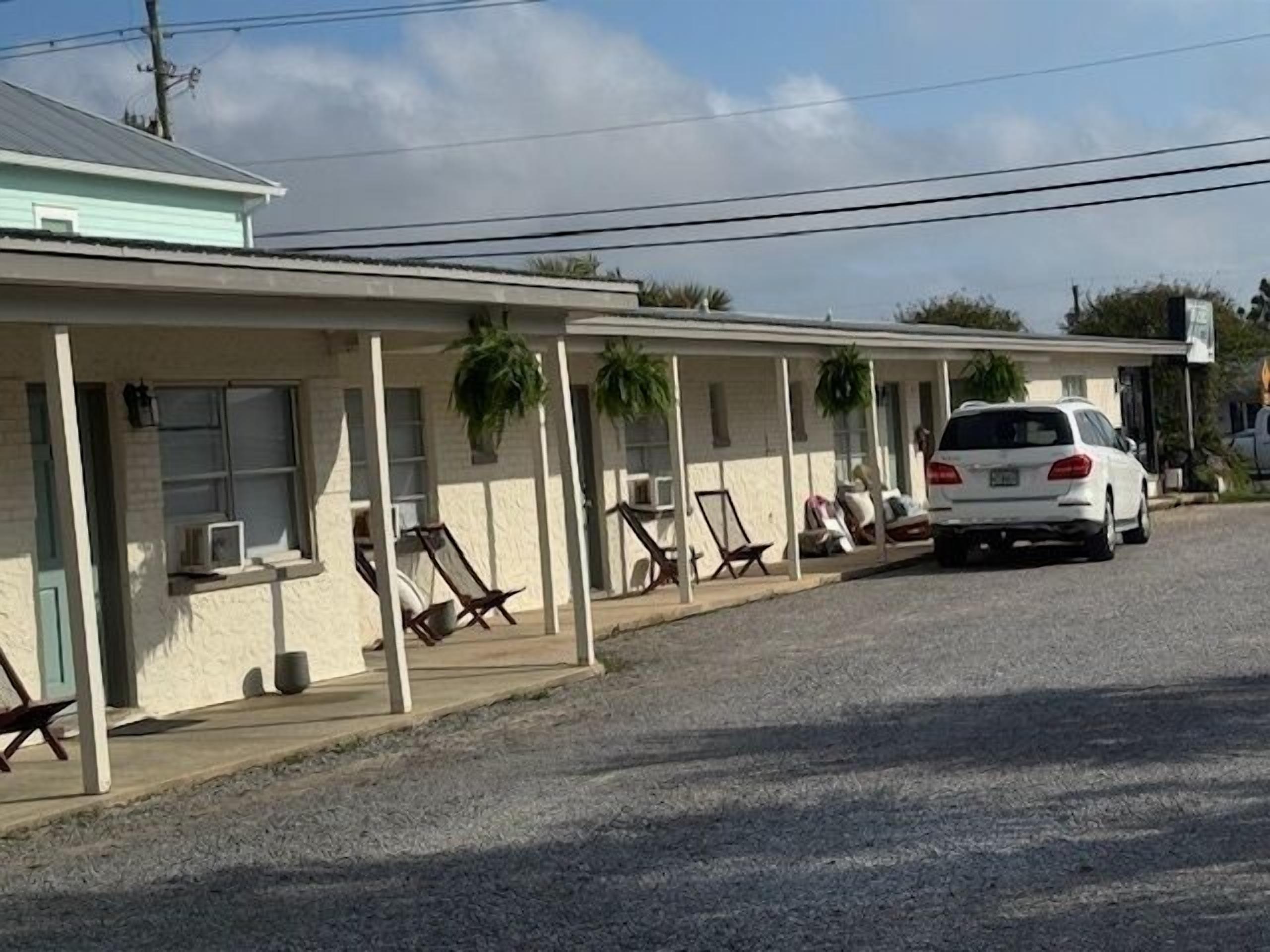 A row of motel rooms with individual air conditioning units, a white car parked in front, and a clear sky.