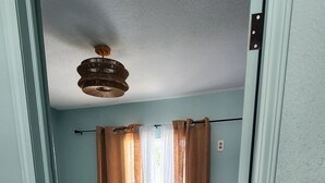 A bedroom with a bed, curtains, a ceiling fan, and a door.