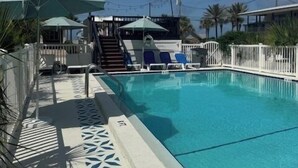 A swimming pool with a white deck, sun umbrellas, and lounge chairs.