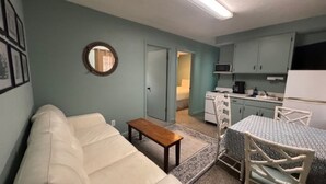 Une pièce de taille modeste comprenant un lit, une petite table, un coin cuisine et une salle de bain visible à travers une porte ouverte.