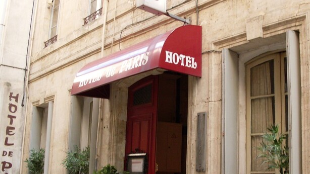 A hotel entrance with a red awning, a red door, and potted plants on the ground floor. - Hôtel de Paris (Narbonne)