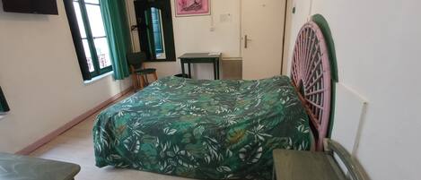 A bedroom with a bed, a chair, a small table, a mirror, and a door.