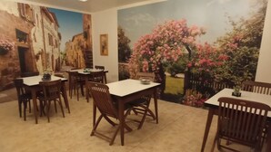 A dining area with multiple tables and chairs, a mural of a street scene, and a garden view. - Hôtel de Paris (Narbonne)