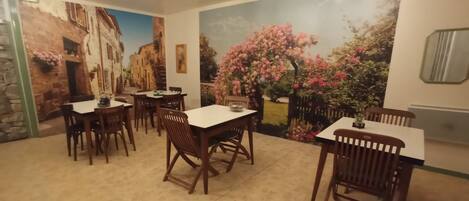 Comedor con varias mesas y sillas, un mural que representa una escena callejera y vistas a un jardín.