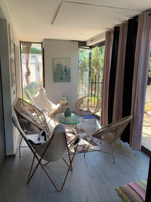 Une chambre moderne avec une table en verre, des chaises en osier et une vue sur la verdure environnante.