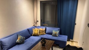 Een moderne woonkamer met een blauwe hoekbank, een houten salontafel en een kamerbreed tapijt met dessin.