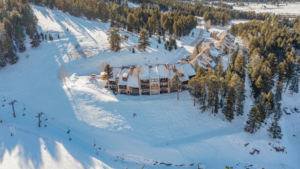 A snow-covered lodge with a ski lift in the foreground, surrounded by dense forest. - Cozy ski in ski out studio in Angel Fire!  (Angel Fire)